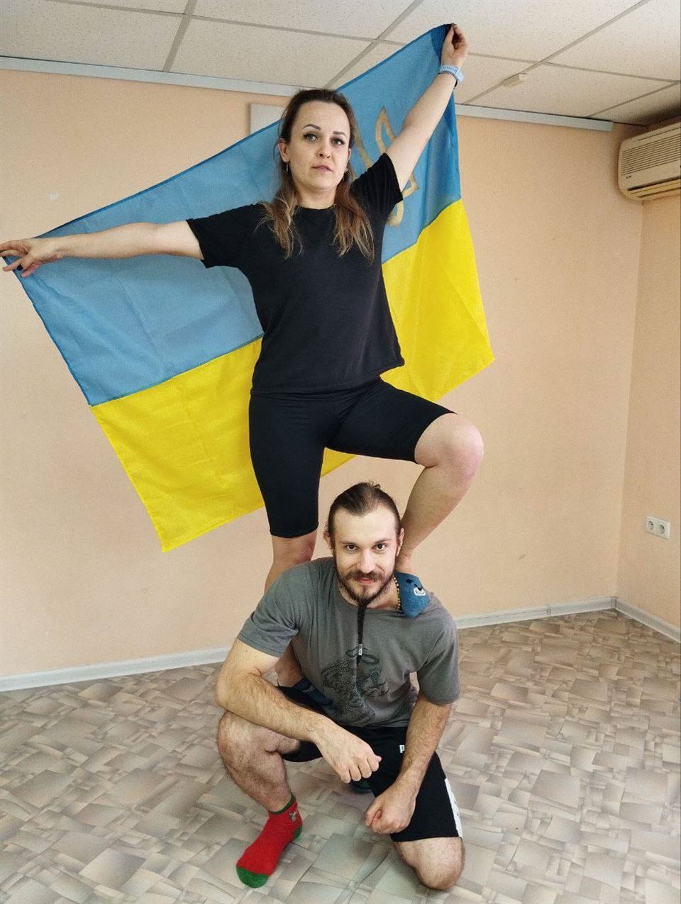 Двоє дорослих тренуються на тлі українського прапора