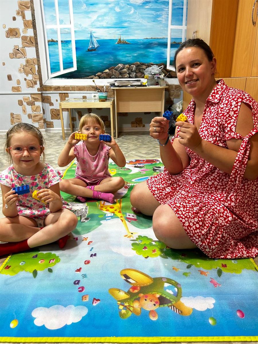 Педагог із двома дівчатками на ігровому килимку в загальному кабінеті