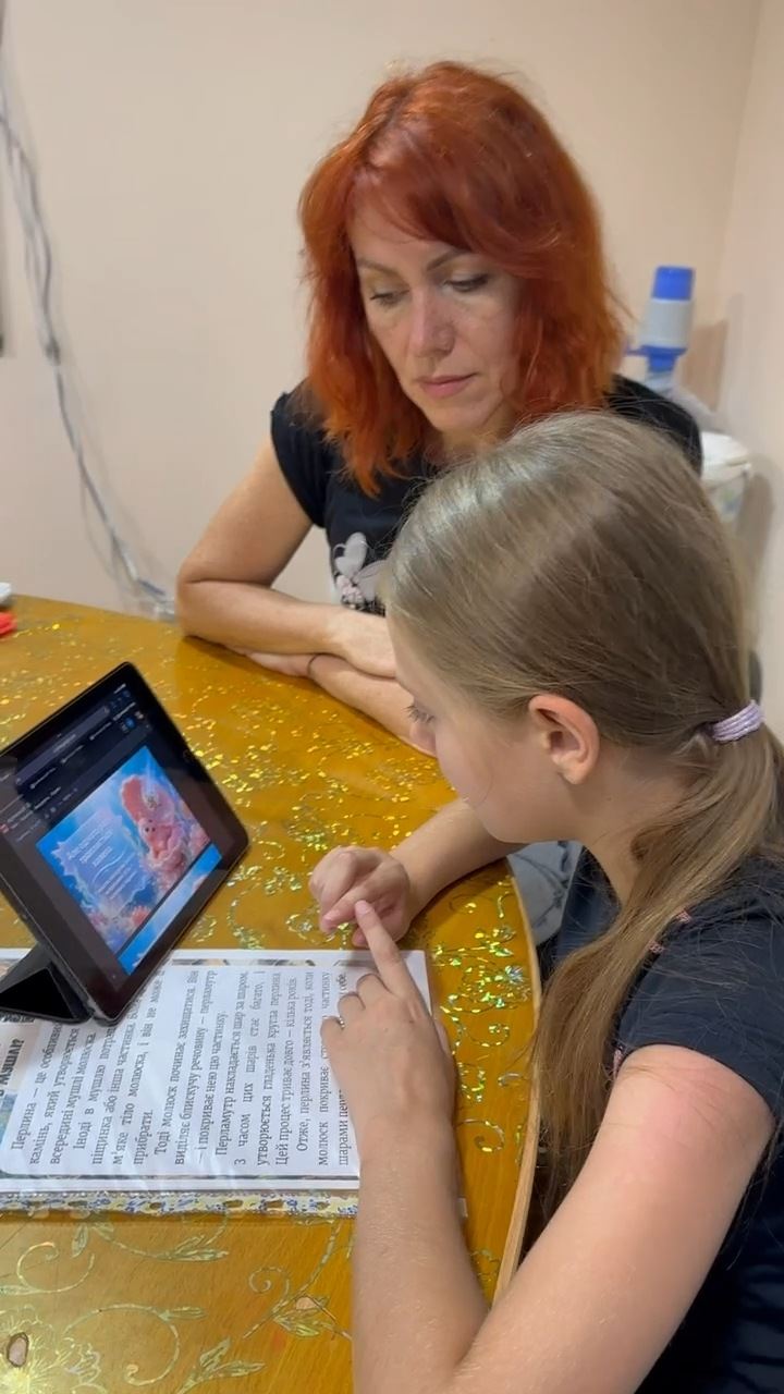 Викладачка з дівчинкою за столом: завдання на аркуші й планшет